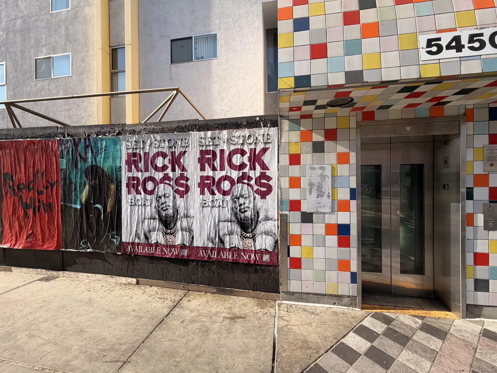 Rick Ross posters beside a facade with multicolored tiles